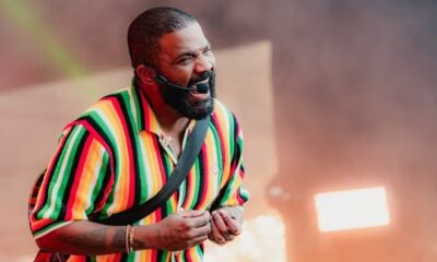 Homem negro barbudo com camisa listrada colorida cantando em microfone headset no palco