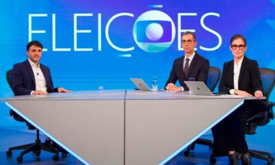 Três apresentadores em estúdio de TV com tela azul exibindo "ELEIÇÕES" e logo da Globo ao fundo