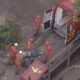 Seis bombeiros em uniformes laranja resgatam homem ferido em maca para ambulância