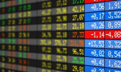 Painel digital da bolsa de valores exibindo cotações e variações em vermelho, azul, verde e amarelo