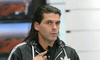 Homem de cabelo comprido e jaqueta preta Adidas gesticula enquanto fala