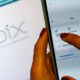 Mãos com unhas vermelhas usando smartphone com aplicativo Pix, e logo Pix no fundo