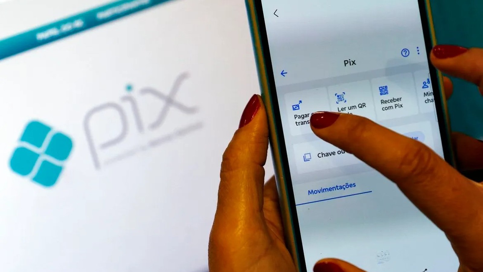 Mãos com unhas vermelhas usando smartphone com aplicativo Pix, e logo Pix no fundo