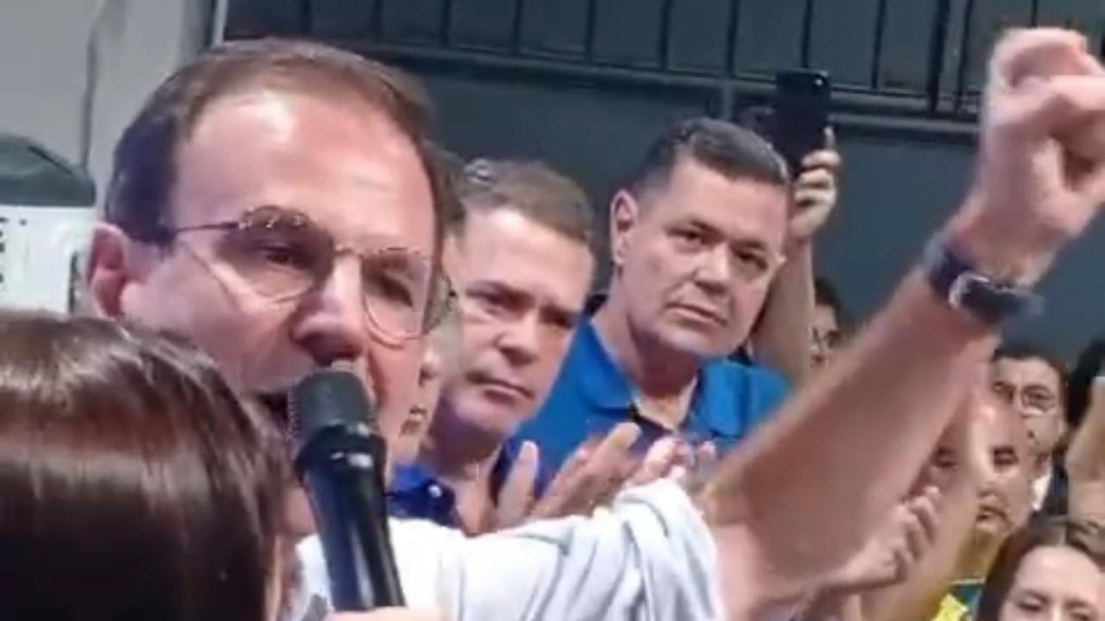 Eduardo Paes, de óculos, fala ao microfone enquanto apoiadores levantam o punho e aplaudem