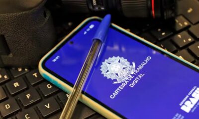 Smartphone exibe app "Carteira de Trabalho Digital" com brasão e caneta azul em teclado