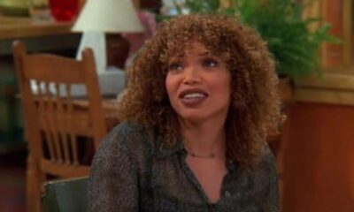 Tisha Campbell com cabelo cacheado, blusa estampada, sorrindo e olhando para o lado.