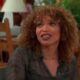 Tisha Campbell com cabelo cacheado, blusa estampada, sorrindo e olhando para o lado.