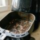Cesta suja de air fryer com restos de comida e gordura, sendo removida da base