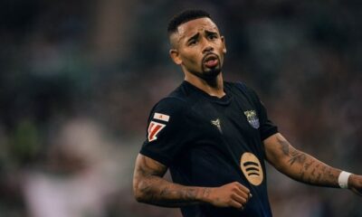 Gabriel Jesus em campo, camisa escura de futebol, barba, tatuagens, boca semiaberta