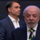 Lula em primeiro plano falando, Flávio Bolsonaro atrás, em debate com hashtag #DebateNaBand