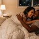 Casal sorridente e abraçado na cama, deitados sob um edredom branco, à noite em um quarto