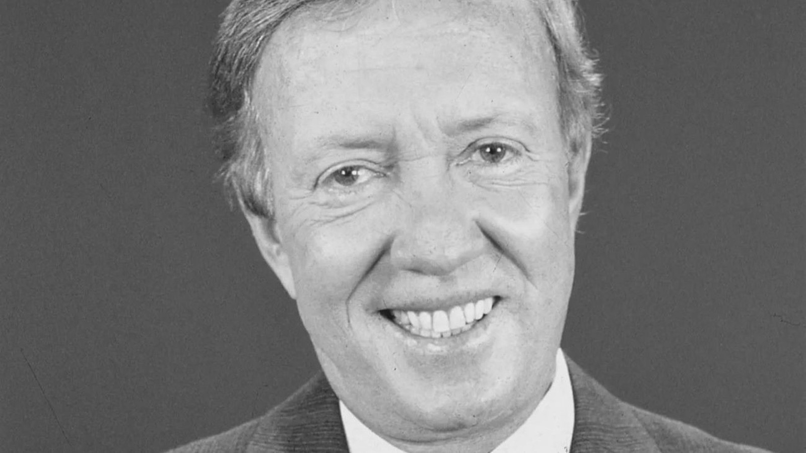 Retrato em preto e branco de Roberto Maya, homem sorridente com terno e camisa branca
