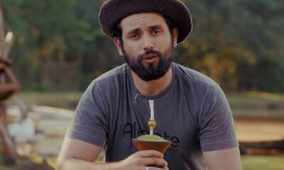 Matteus Amaral com chapéu, camiseta cinza "Alegrete Matteus", barba, segurando chimarrão em área rural