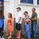 Pessoas em fila do lado de fora de um local de votação, uma oficial com colete TRERJ