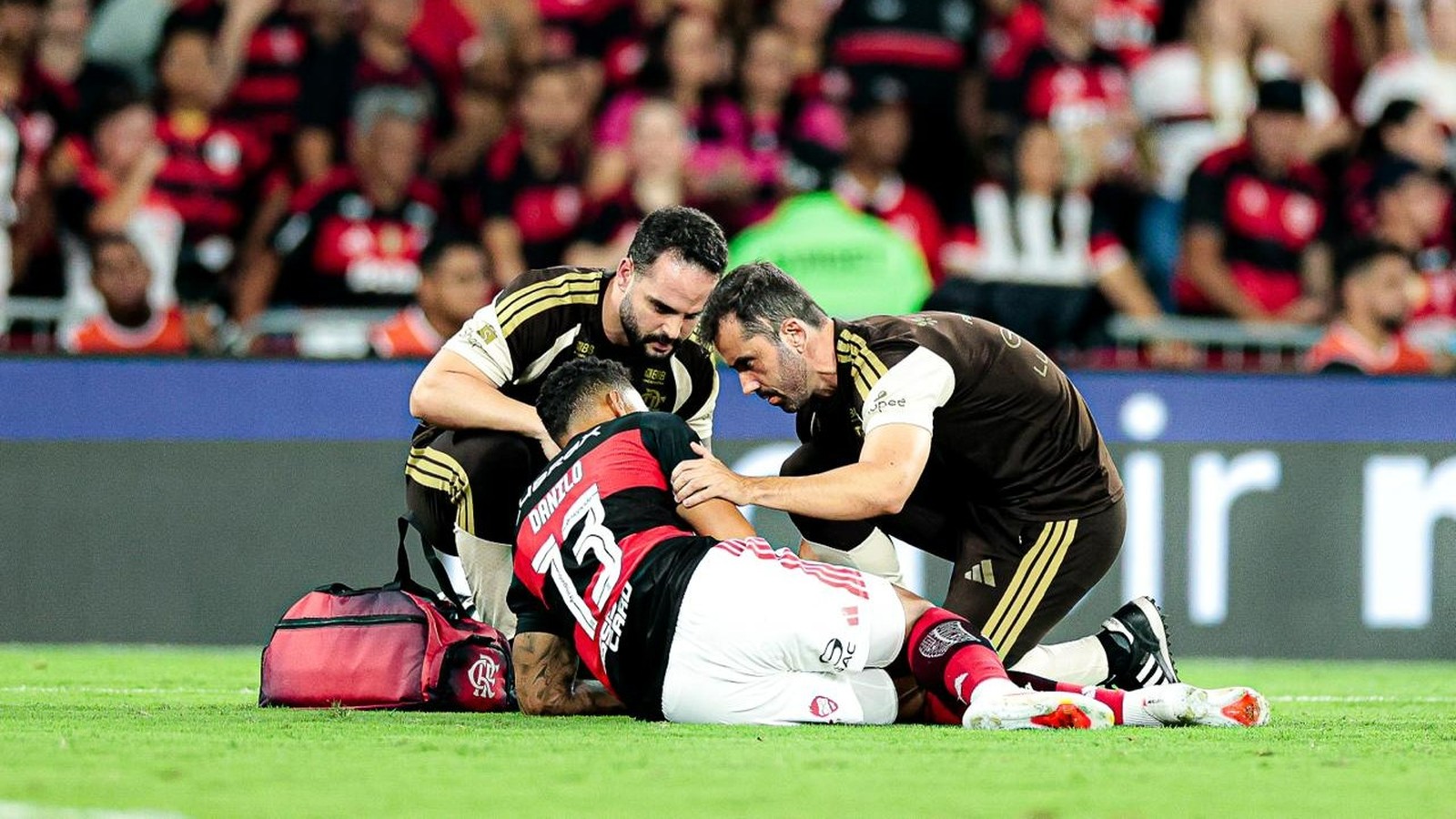 Jogador Danilo (camisa 13) deitado no gramado, atendido por dois médicos em campo de futebol
