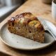 Fatia de bolo de banana caramelizada em prato com garfo e xícara de café em mesa de madeira