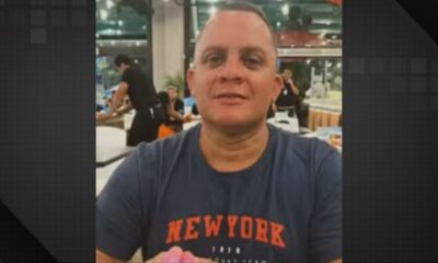 Homem de meia-idade, careca, camiseta azul escura com "NEWYORK" em laranja, sorrindo