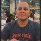 Homem de meia-idade, careca, camiseta azul escura com "NEWYORK" em laranja, sorrindo