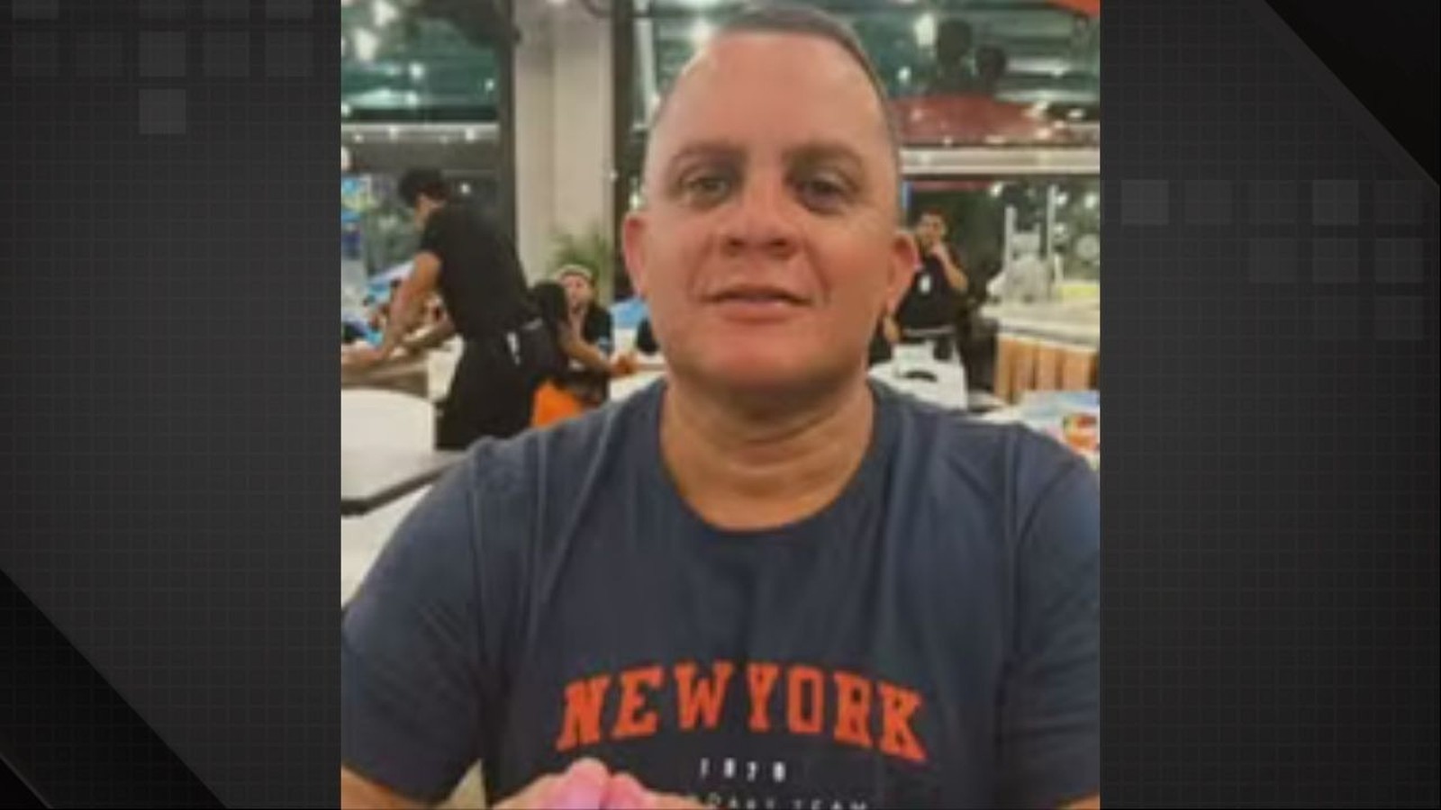 Homem de meia-idade, careca, camiseta azul escura com "NEWYORK" em laranja, sorrindo