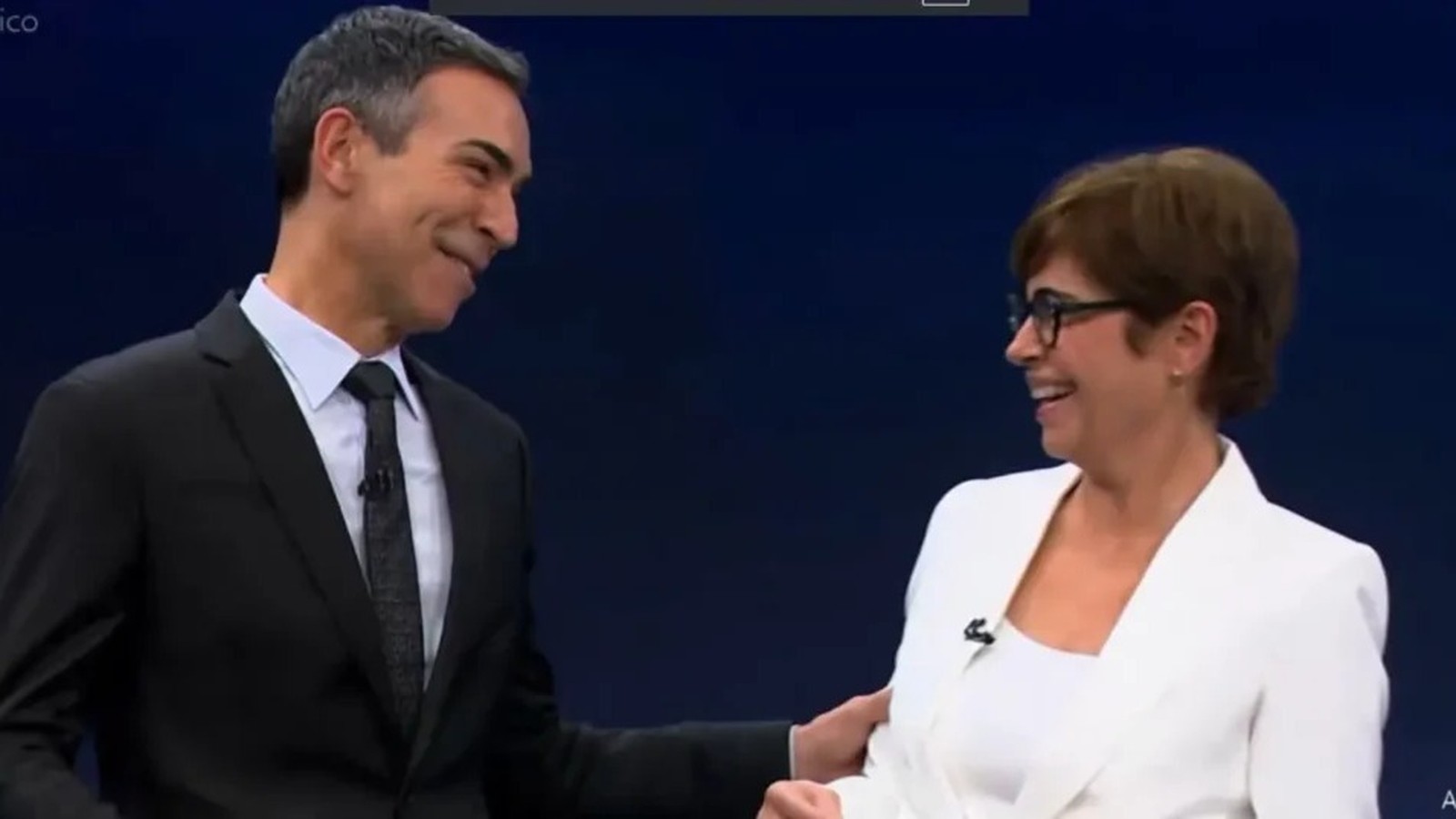 César Tralli e Renata Vasconcellos sorrindo um para o outro em estúdio de TV