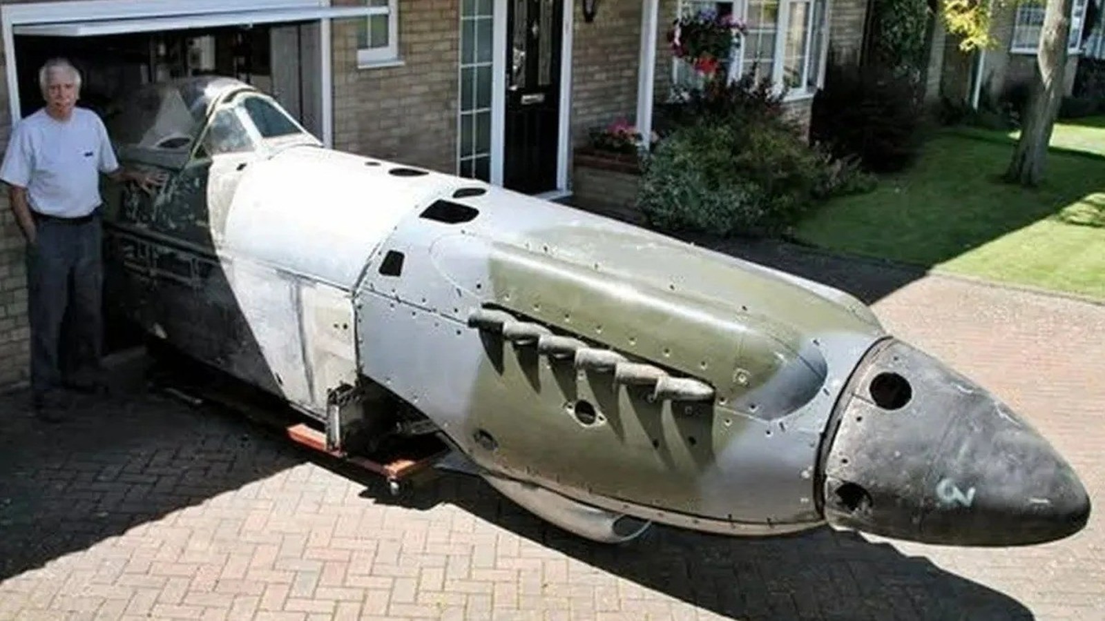 Peter Arnold ao lado da fuselagem de um caça Spitfire dentro de uma garagem