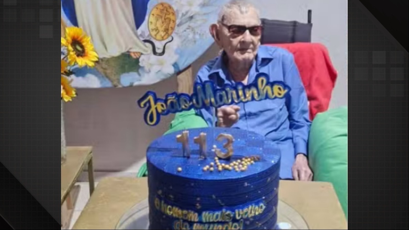 Homem de óculos e camisa azul com bolo azul escrito '113' e 'João Marinho'