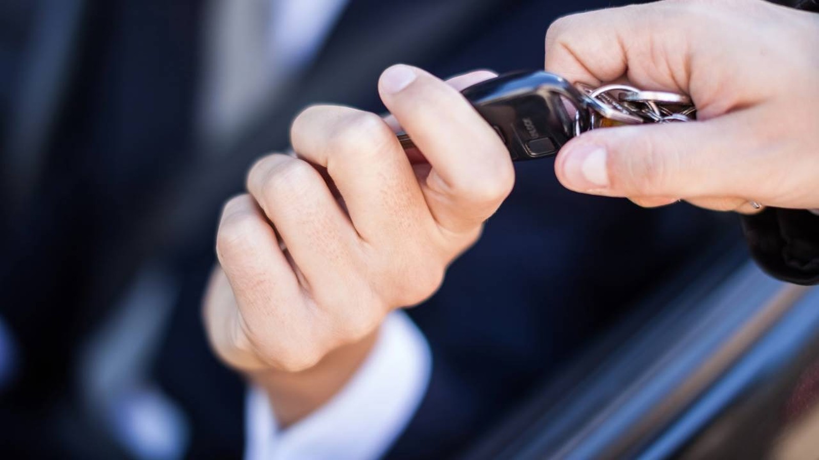 Duas mãos seguram um chaveiro de carro preto com a palavra 'UNLOCK' visível