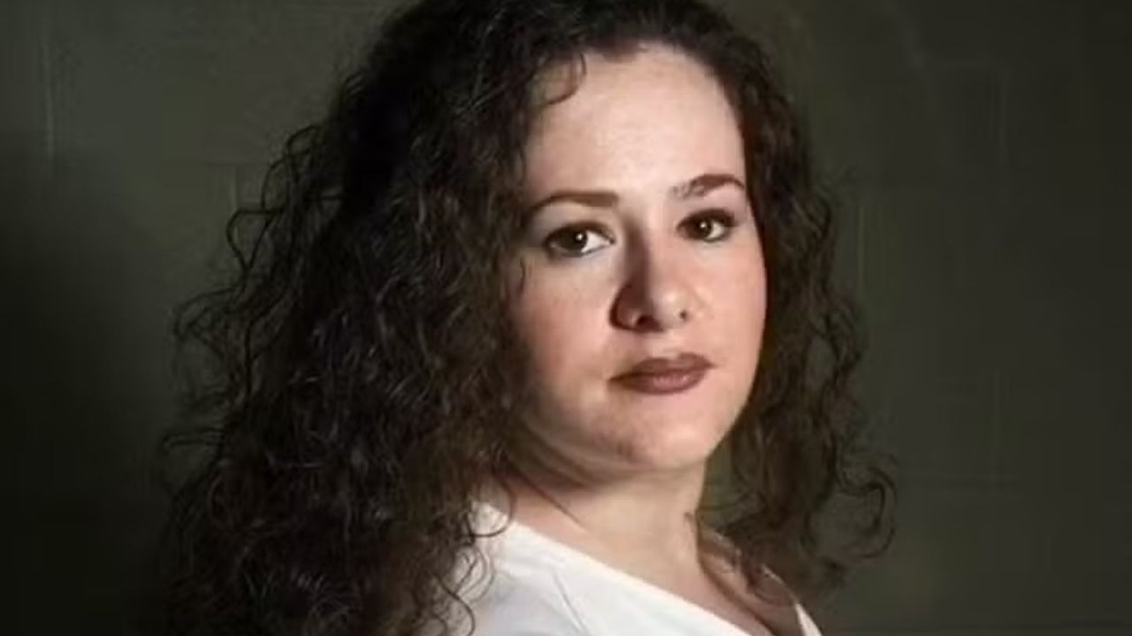 Close-up de mulher com cabelos cacheados escuros, olhos castanhos e expressão séria