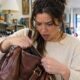 Mulher com expressão de surpresa olha dentro de bolsa marrom em brechó.