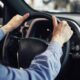 Mãos de pessoa em camisa azul segurando volante de carro com painel e botões AUTO OFF