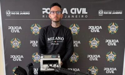 Gustavo Gonçalves Porto Melo em frente a fundo da Polícia Civil, com máquina de contar dinheiro e fuzil