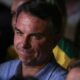 Close-up de Flávio Bolsonaro, cabelo escuro, camisa azul, rosto sério, olhando para o lado.