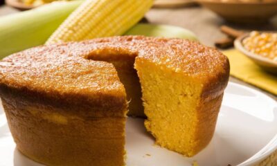 Bolo de fubá amarelo com fatia cortada, casca dourada, milho fresco e grãos na mesa