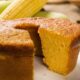 Bolo de fubá amarelo com fatia cortada, casca dourada, milho fresco e grãos na mesa