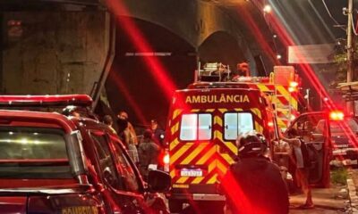 Ambulância vermelha e carros de bombeiros com luzes piscando em local de acidente à noite