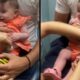 Bebê sorridente em vestido laranja tomando vacina no colo, com mãos de profissionais.
