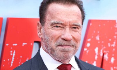 Rosto de Arnold Schwarzenegger em close, sorrindo e usando terno e gravata vermelha