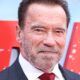 Rosto de Arnold Schwarzenegger em close, sorrindo e usando terno e gravata vermelha