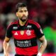 Jogador Lucas Paquetá veste camisa vermelha e preta do Flamengo, olhando focado no campo