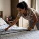 Mulher arruma a cama com lençol estampado, focada, em um quarto com janela