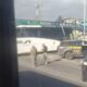 Ônibus branco e duas viaturas da PRF parados em rodovia, com ponte e prédios ao fundo