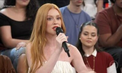 Marina Ruy Barbosa, ruiva, em close, segura microfone preto e fala durante programa de TV