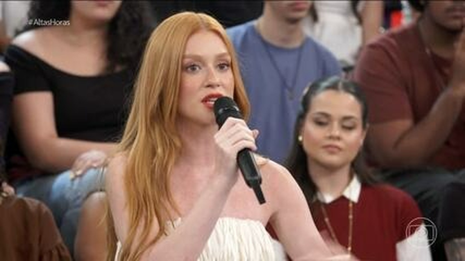 Marina Ruy Barbosa, ruiva, em close, segura microfone preto e fala durante programa de TV