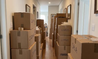 Corredor residencial estreito bloqueado por pilhas de caixas de mudança de papelão rotuladas.