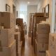 Corredor residencial estreito bloqueado por pilhas de caixas de mudança de papelão rotuladas.