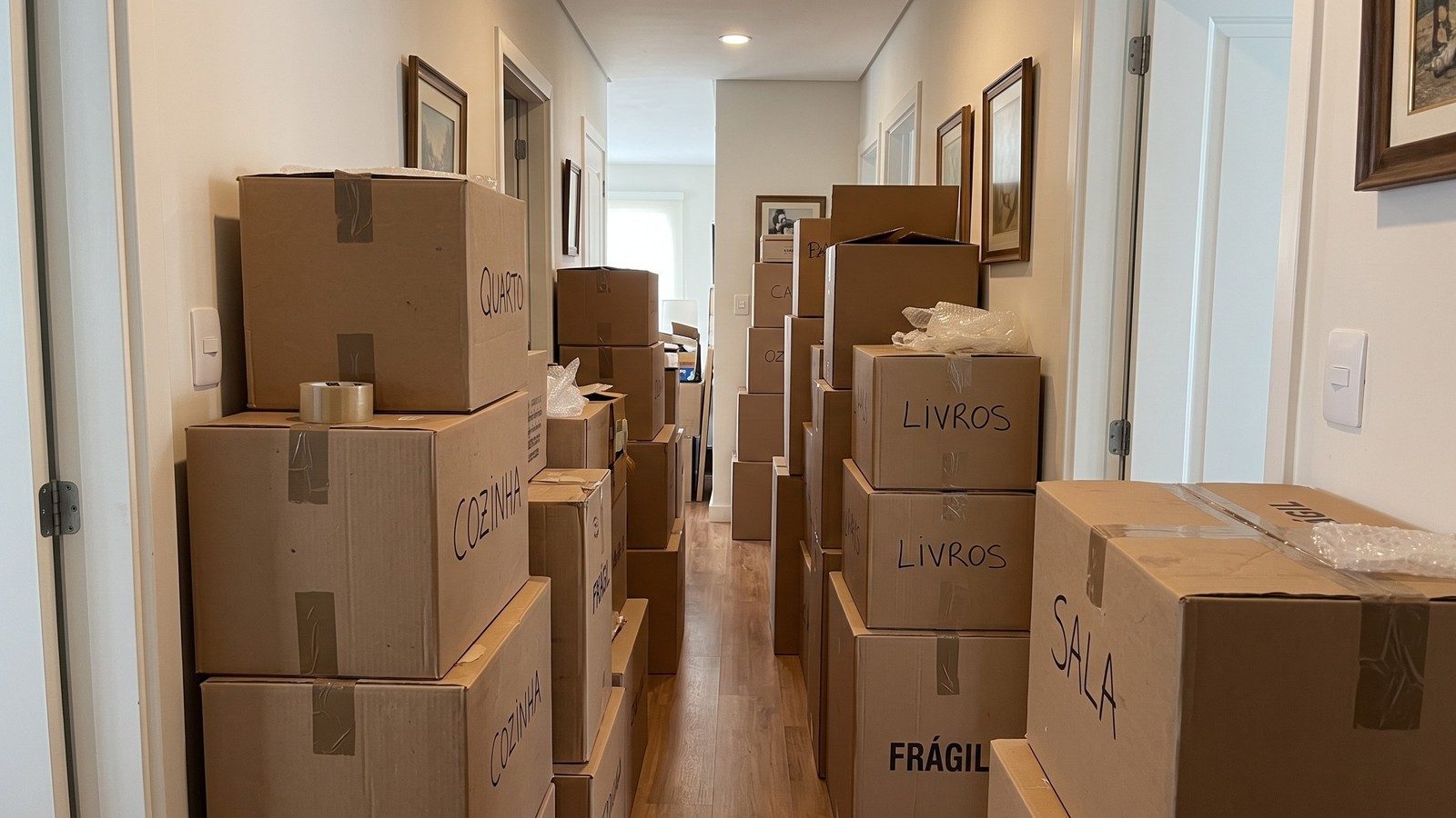 Corredor residencial estreito bloqueado por pilhas de caixas de mudança de papelão rotuladas.