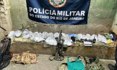 Banner da Polícia Militar do Estado do Rio de Janeiro, sacos de drogas, fuzil, balança, rádio