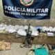 Banner da Polícia Militar do Estado do Rio de Janeiro, sacos de drogas, fuzil, balança, rádio
