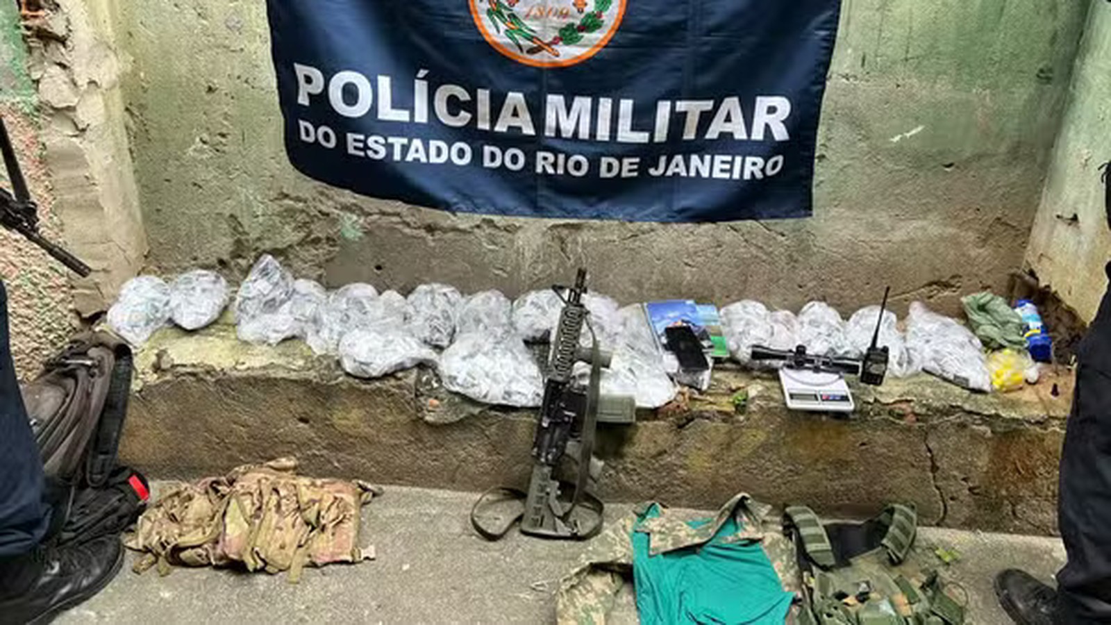 Banner da Polícia Militar do Estado do Rio de Janeiro, sacos de drogas, fuzil, balança, rádio