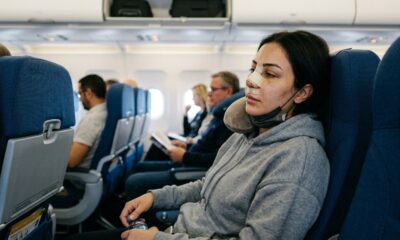 Mulher com bandagens no nariz, máscara e travesseiro de pescoço em assento azul de avião